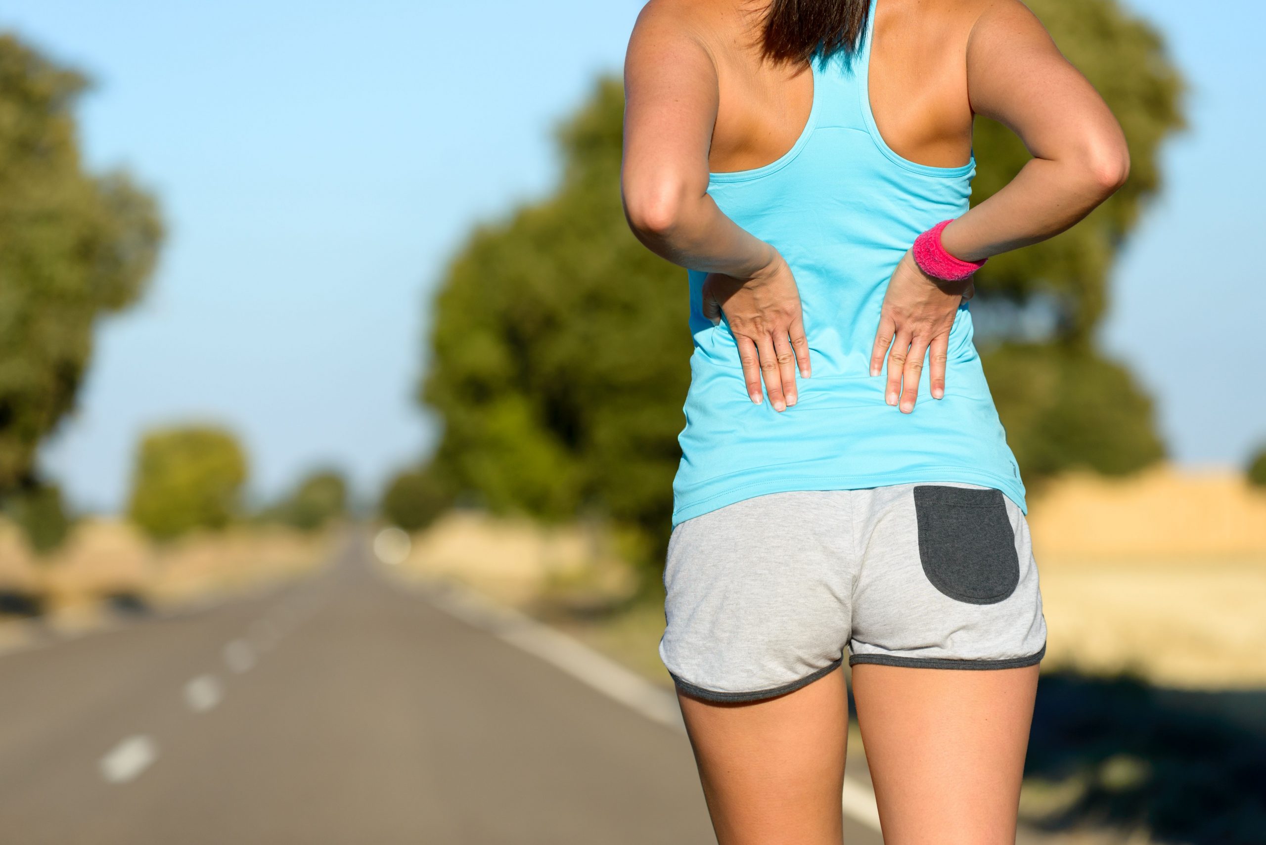 Woman outdoors holding her lower back in discomfort, representing back pain possibly needing chiropractic treatment.